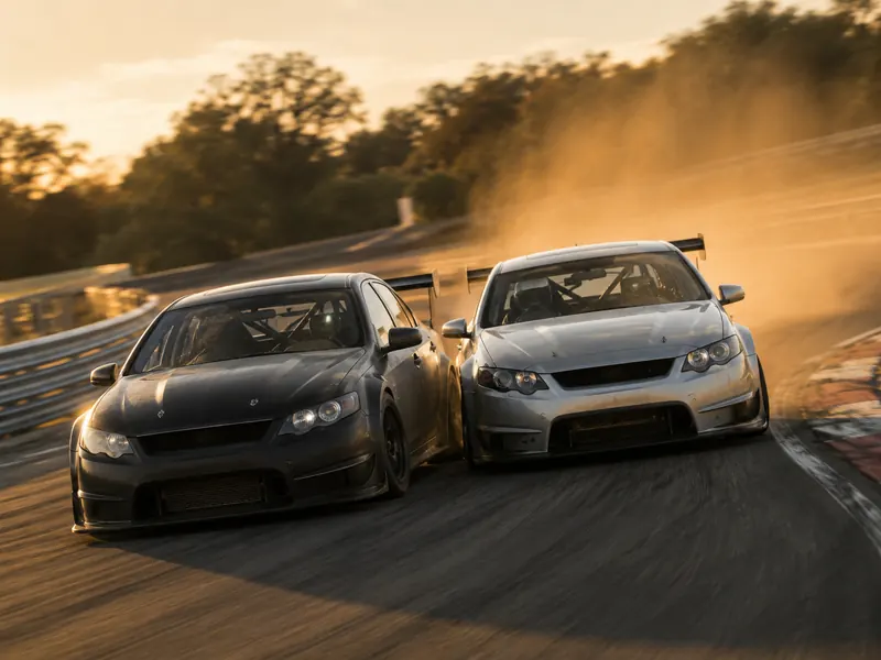 Two touring cars racing side by side through a corner with dust rising off the track